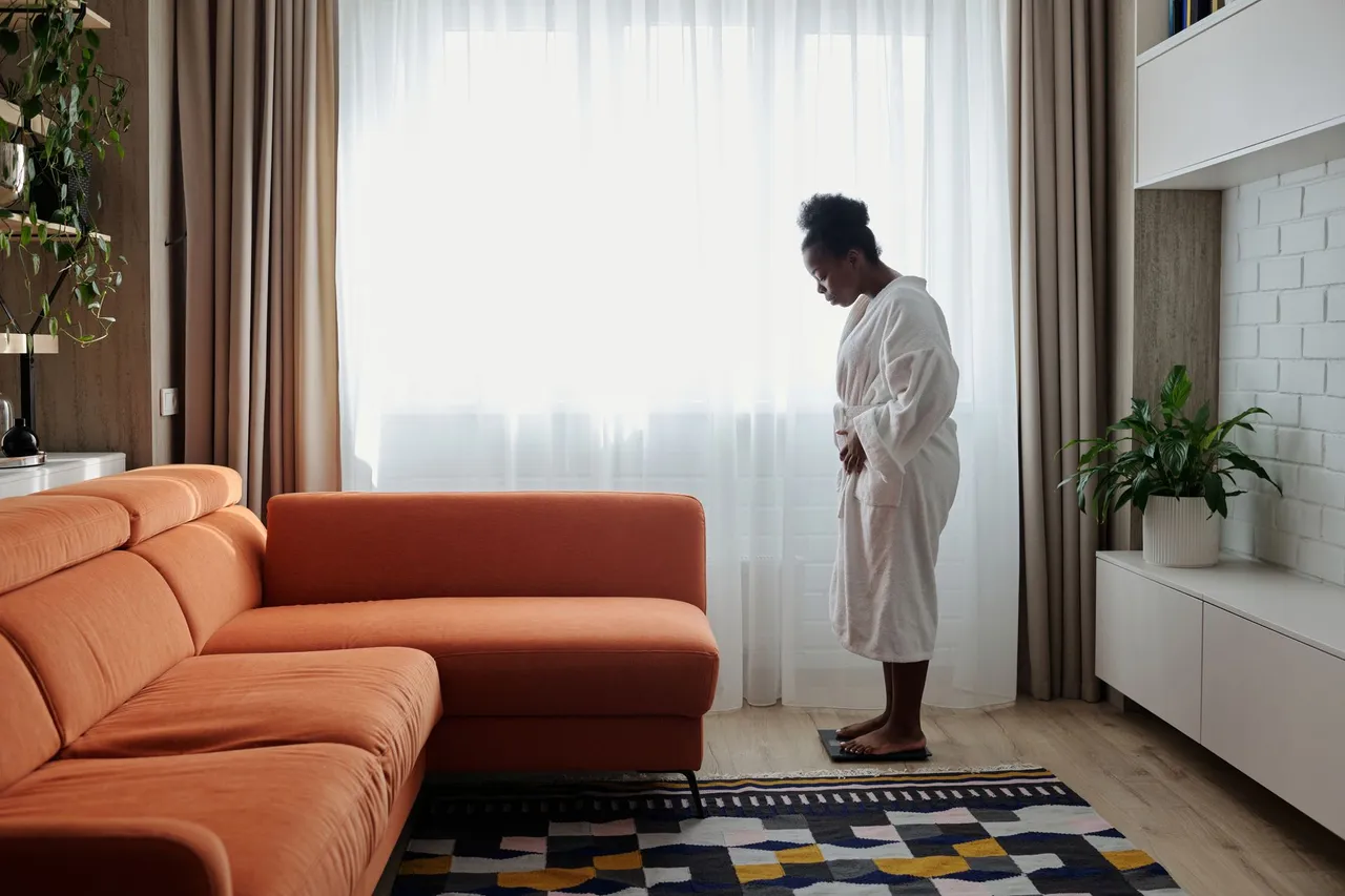 Woman adjusting the thermostat in a bright, contemporary room with large windows and a potted plant.